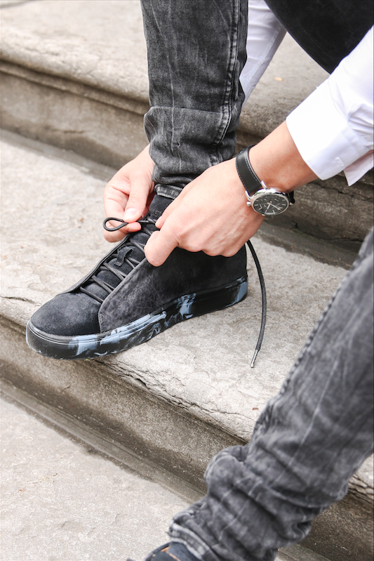 Man bindt zwarte sneakers met marmeren zool vast.